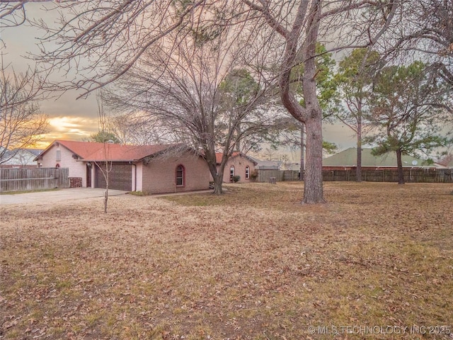 yard at dusk with concrete driveway, fence, and an attached garage