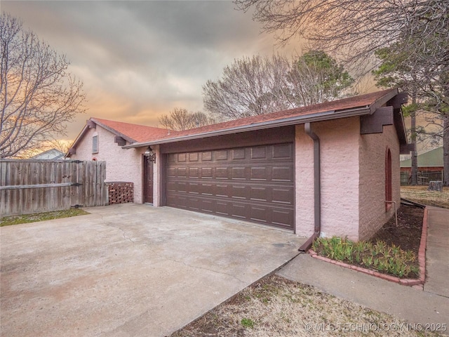 garage at dusk featuring fence