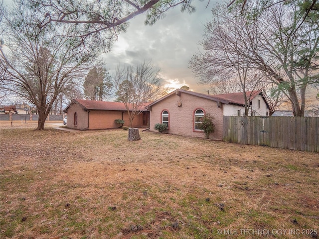 back of house at dusk featuring brick siding and fence