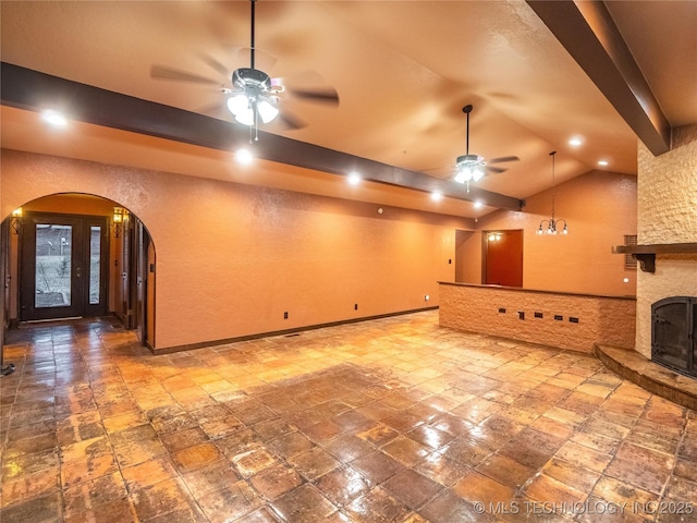 unfurnished living room with arched walkways, vaulted ceiling with beams, a fireplace, a ceiling fan, and baseboards