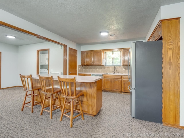 kitchen with sink, a breakfast bar, stainless steel refrigerator, tasteful backsplash, and light carpet