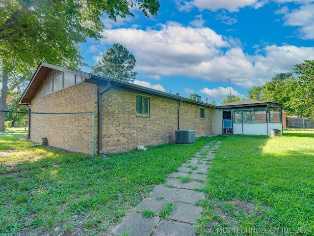 view of home's exterior featuring a sunroom, a lawn, and central air condition unit