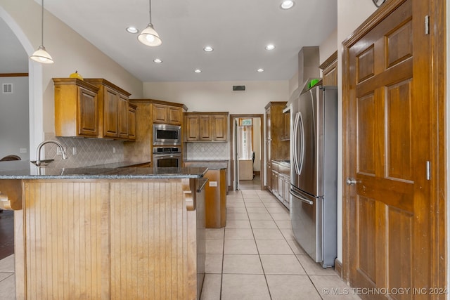 kitchen featuring light tile patterned flooring, tasteful backsplash, stainless steel appliances, dark stone countertops, and a kitchen bar