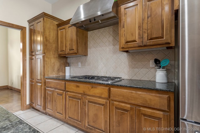 kitchen featuring dark stone countertops, ventilation hood, appliances with stainless steel finishes, light tile patterned floors, and backsplash