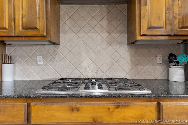 kitchen featuring dark stone countertops, stainless steel gas cooktop, decorative backsplash, and range hood