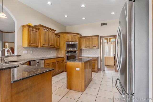 kitchen with dark stone counters, sink, stainless steel appliances, kitchen peninsula, and a center island