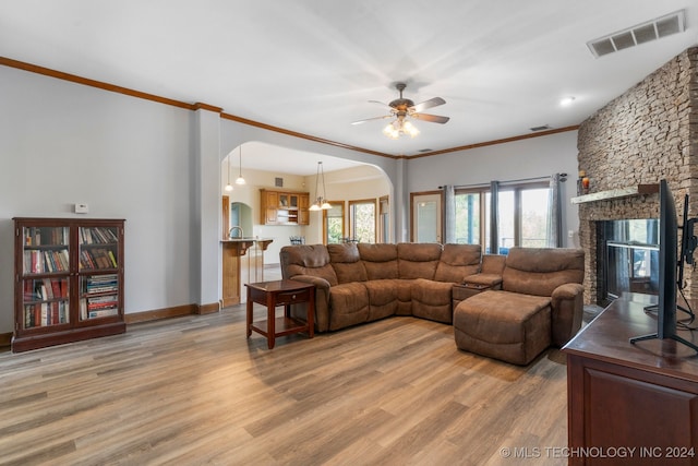 living room featuring wood-type flooring, a stone fireplace, ornamental molding, and ceiling fan