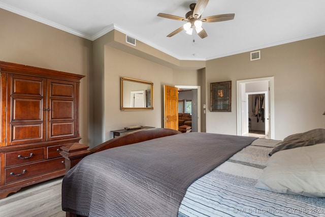 bedroom featuring ceiling fan, crown molding, light hardwood / wood-style floors, and a walk in closet