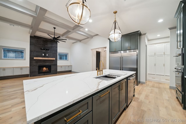 kitchen with appliances with stainless steel finishes, hanging light fixtures, coffered ceiling, light stone counters, and a center island with sink