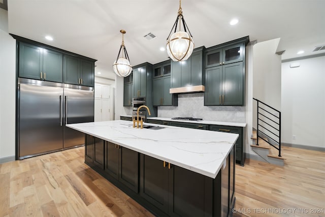 kitchen with hanging light fixtures, a kitchen island with sink, sink, light hardwood / wood-style floors, and stainless steel appliances