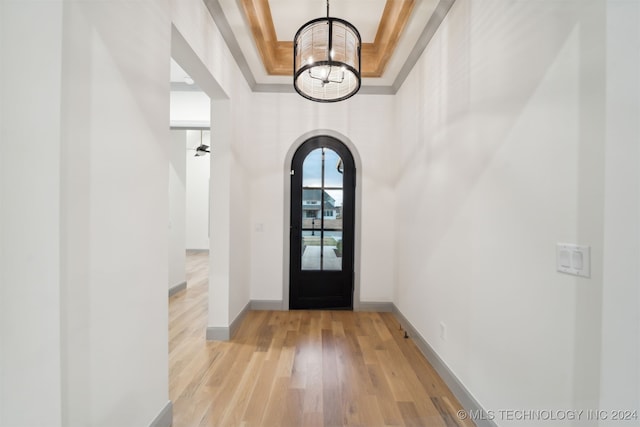 entryway with a towering ceiling, a tray ceiling, and light hardwood / wood-style floors