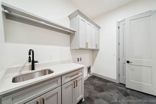 laundry area featuring electric dryer hookup, washer hookup, dark tile patterned flooring, sink, and cabinets