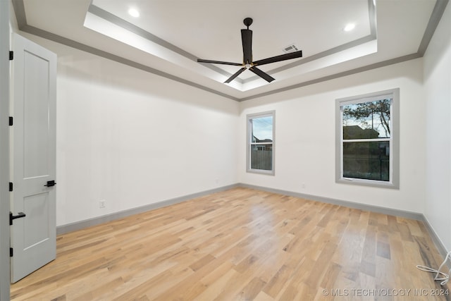 empty room featuring ceiling fan, a tray ceiling, and light wood-type flooring