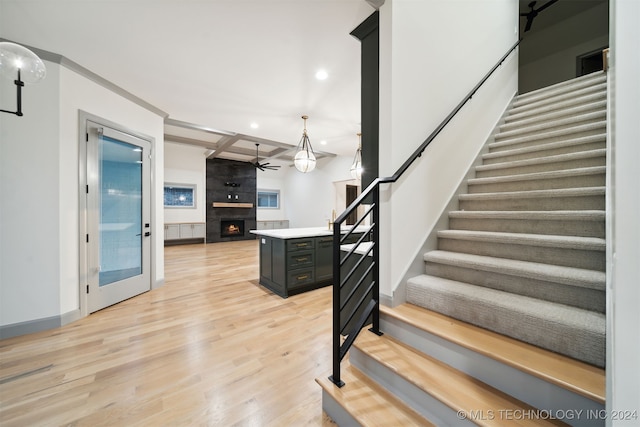 stairway with ceiling fan, hardwood / wood-style flooring, crown molding, and a fireplace