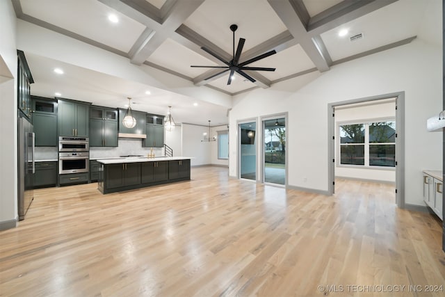 kitchen with beam ceiling, hanging light fixtures, a kitchen island with sink, light wood-type flooring, and stainless steel appliances