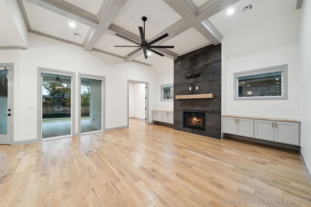 unfurnished living room with beamed ceiling, a tiled fireplace, and light hardwood / wood-style floors