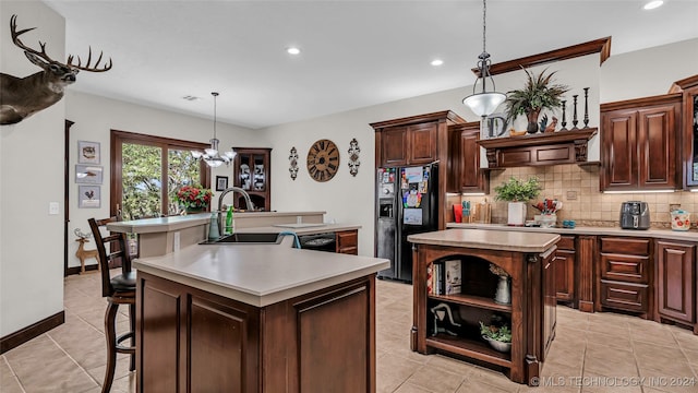 kitchen featuring sink, black appliances, decorative backsplash, a center island with sink, and decorative light fixtures