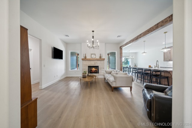 living room featuring an inviting chandelier, a stone fireplace, light hardwood / wood-style floors, and plenty of natural light