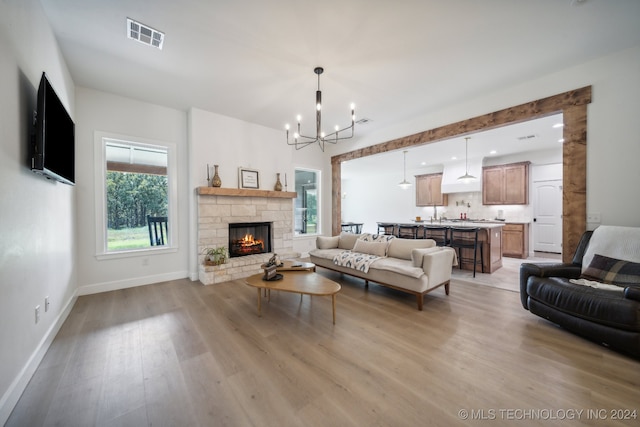 living room with a chandelier, a fireplace, and light hardwood / wood-style floors