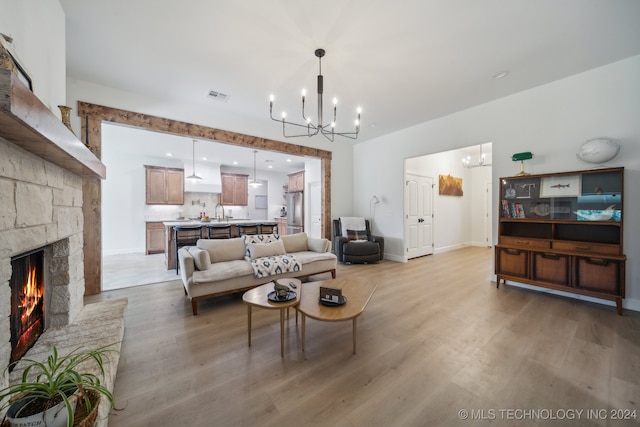 living room featuring a notable chandelier, a stone fireplace, and light wood-type flooring