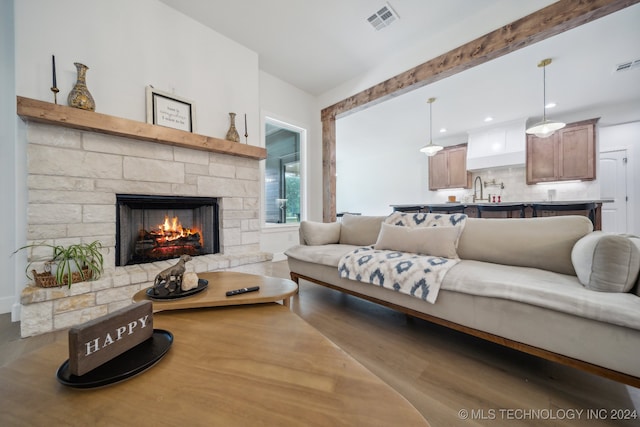 living room with a stone fireplace, beam ceiling, sink, and wood-type flooring