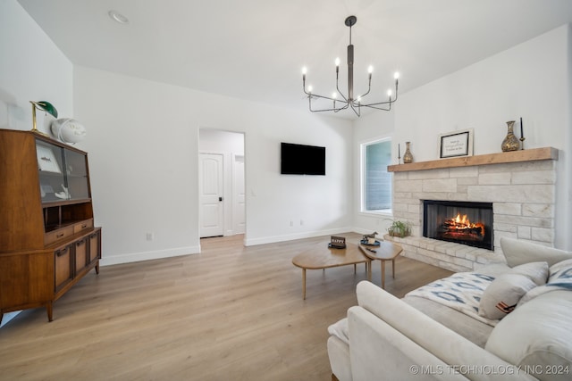 living room featuring light hardwood / wood-style floors, an inviting chandelier, and a stone fireplace