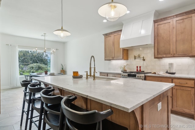 kitchen featuring decorative backsplash, an island with sink, hanging light fixtures, light stone countertops, and custom exhaust hood