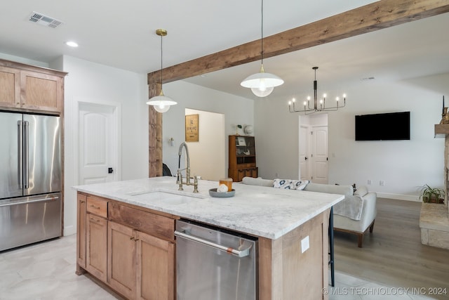 kitchen with hanging light fixtures, light stone counters, a kitchen island with sink, stainless steel appliances, and sink