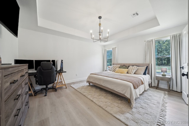 bedroom featuring multiple windows, light wood-type flooring, and a raised ceiling