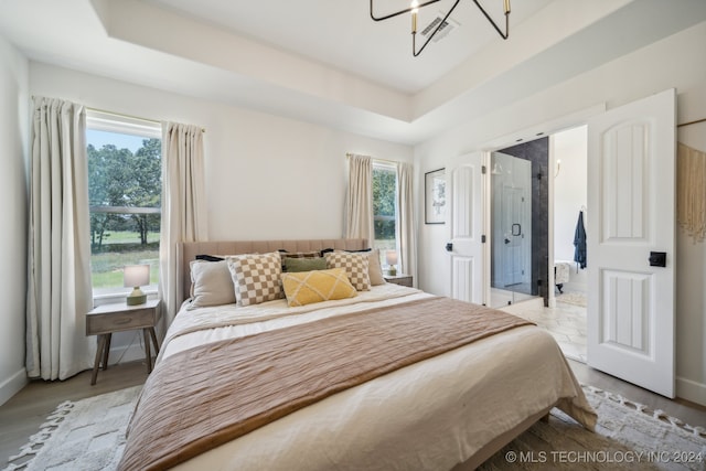 bedroom featuring light hardwood / wood-style flooring, multiple windows, and a tray ceiling