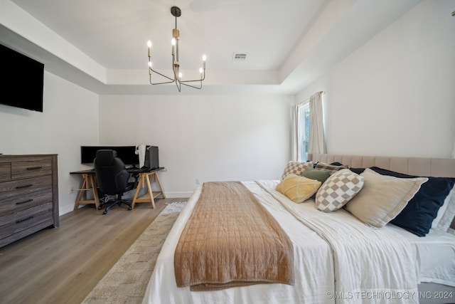 bedroom featuring a notable chandelier, hardwood / wood-style flooring, and a tray ceiling