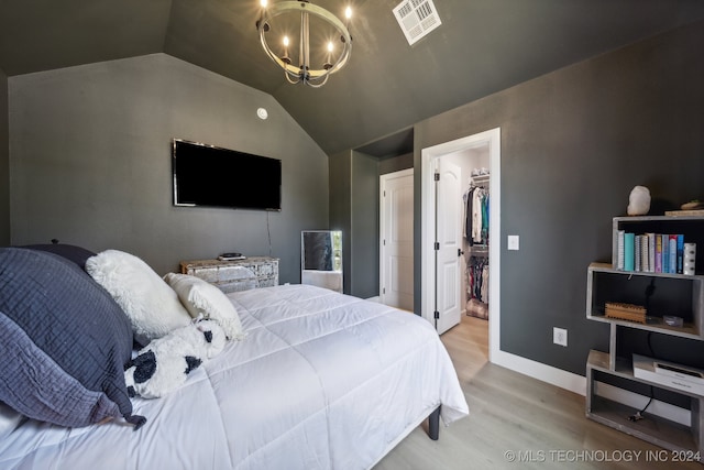 bedroom with a spacious closet, a closet, light hardwood / wood-style floors, lofted ceiling, and an inviting chandelier