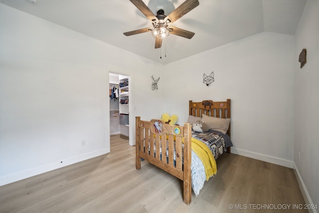 bedroom featuring a walk in closet, a closet, ceiling fan, lofted ceiling, and light hardwood / wood-style flooring