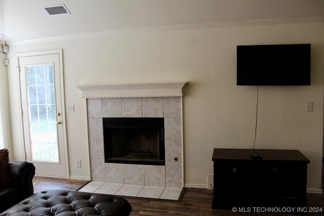 living room with ornamental molding, wood-type flooring, and a tiled fireplace