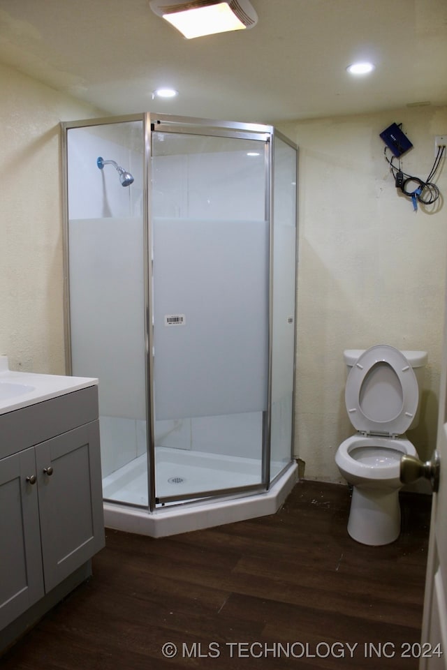 bathroom featuring hardwood / wood-style flooring, a shower with shower door, toilet, and vanity