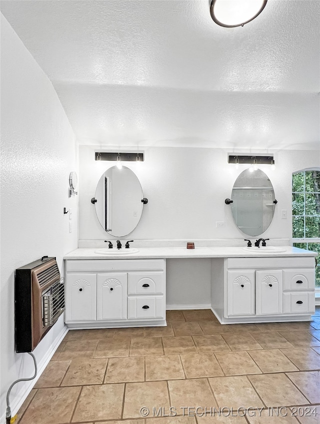 bathroom with a textured ceiling, dual vanity, tile patterned floors, and heating unit