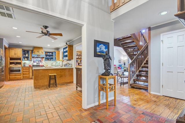 kitchen featuring premium range hood, appliances with stainless steel finishes, a kitchen bar, ornamental molding, and kitchen peninsula