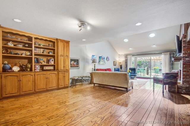 bedroom with vaulted ceiling, access to outside, a textured ceiling, and light hardwood / wood-style flooring