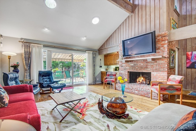 living room featuring high vaulted ceiling, wood walls, light wood-type flooring, a brick fireplace, and beam ceiling