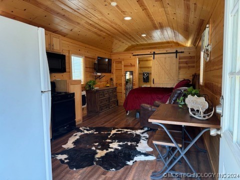 bedroom featuring a barn door, dark hardwood / wood-style floors, wooden walls, and white refrigerator