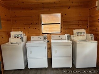 clothes washing area featuring washing machine and clothes dryer, wood walls, and dark hardwood / wood-style flooring