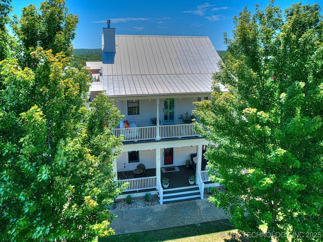 view of front of house with a chimney, covered porch, a standing seam roof, metal roof, and a balcony