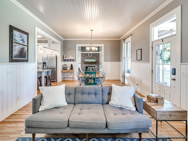 living area with an inviting chandelier, ornamental molding, wood ceiling, wainscoting, and light wood-type flooring