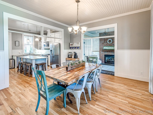 dining space with ornamental molding, a wainscoted wall, light wood finished floors, and an inviting chandelier