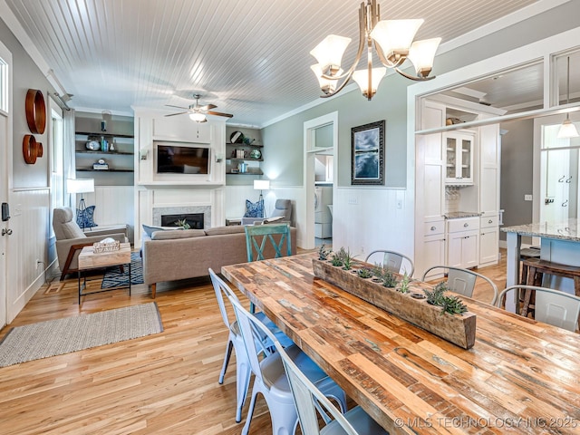 dining space featuring a fireplace, ornamental molding, light wood-style floors, wainscoting, and wooden ceiling