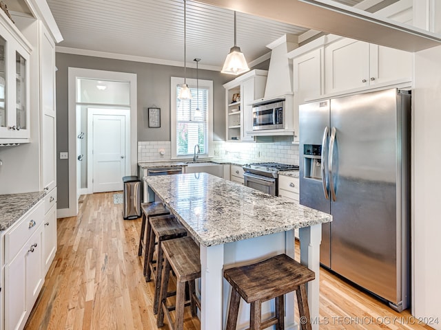 kitchen with appliances with stainless steel finishes, a kitchen island, white cabinetry, light stone counters, and ornamental molding