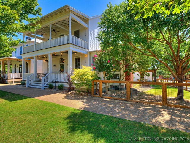 view of front facade featuring ceiling fan, a porch, a balcony, fence, and a front lawn