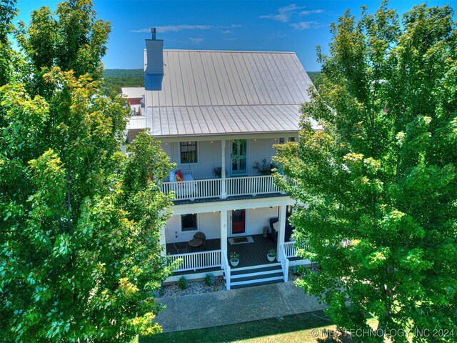 view of front facade with a chimney, a porch, a standing seam roof, metal roof, and a balcony