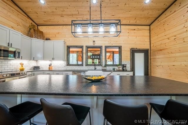 kitchen with wood walls, appliances with stainless steel finishes, a kitchen bar, and vaulted ceiling