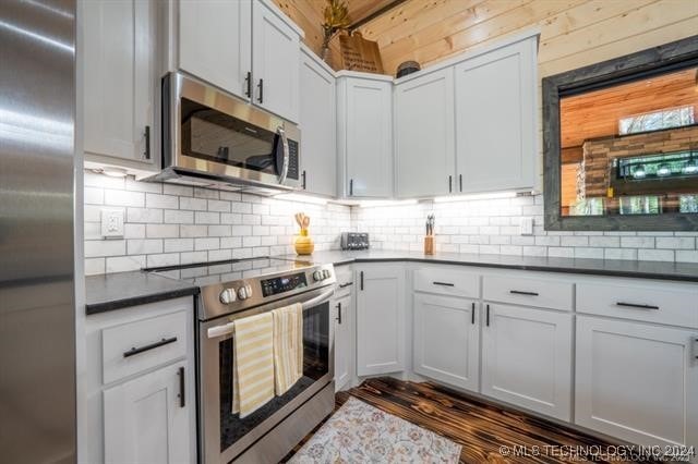 kitchen with dark hardwood / wood-style floors, backsplash, appliances with stainless steel finishes, and white cabinets